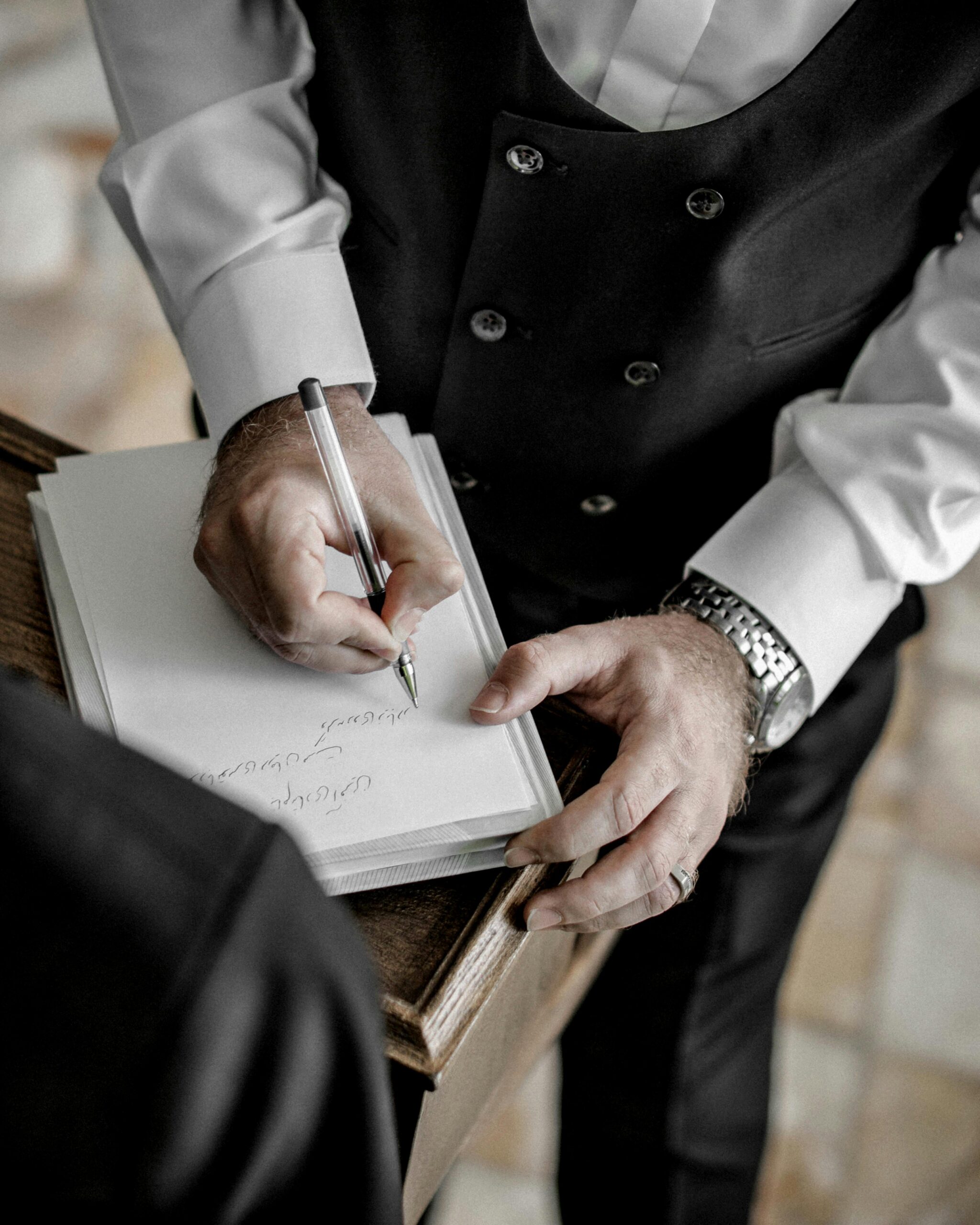 Close-up of a man in formal attire signing a document during a wedding ceremony.